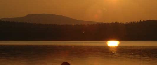 Norwegen -Blick gegen die untergehende Sonne, auf Mann im Schneidersitz am Seeufer