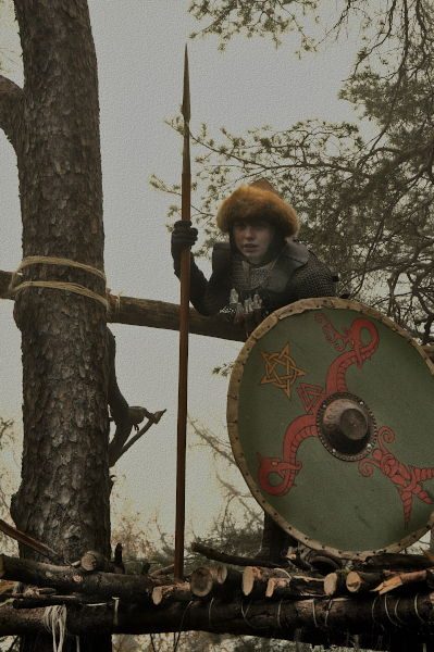 Auf einem Holzpodest im Wald steht ein Krieger mit Schild und Schwert