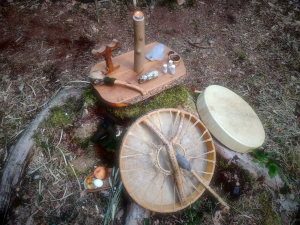 Einfacher Altar mit Kerze, Räucherwerk und Trommeln auf einem Baumstumpf im Wald